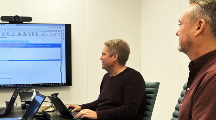 Roy Ulvang og Asbjørn Solberg-Eriksen sitter ved et bord, foran en stor skjerm der portalen Mercell er synlig.